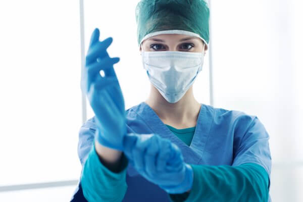 Female surgeon preparing for the surgical operation, she is wearing medical exam gloves and looking at camera