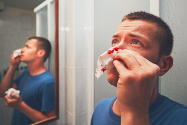 Man with nosebleed in bathroom. For themes of illness, injury or violence.