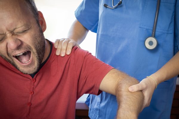 Nurse or other medical professional examining the dislocated shoulder of a patient, who is screaming in pain.